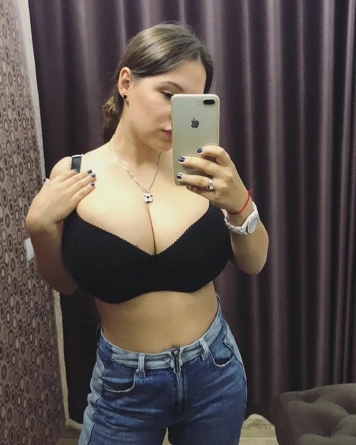 Femme arabe aux cheveux bruns, en sous-vêtements roses, prenant un selfie devant un miroir dans une salle de bain.