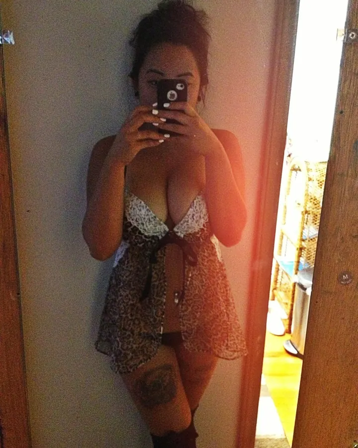 Femme arabe aux cheveux bruns, en maillot de bain orange, debout devant un lit, les mains sur les hanches.